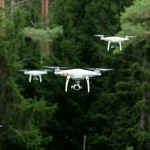 Fotografia dinamica con teleobiettivo zoom (200mm) di uno sciame di droni che eseguono una manovra coordinata di evitamento ostacoli in un ambiente esterno complesso come una foresta fitta. Alta velocità dell'otturatore per congelare il movimento dei droni, tracciamento del movimento attivo che segue lo sciame, luce naturale filtrata dagli alberi.
