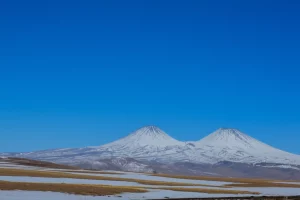 Imponente veduta del Monte Hasan, stratovulcano turco, con le sue due cime distinte sotto un cielo azzurro intenso, pendici parzialmente innevate, fotografia paesaggistica con obiettivo grandangolare 20mm, focus nitido sull'intera montagna, luce solare diretta.