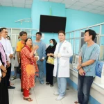 Immagine fotorealistica che mostra un gruppo diversificato di persone, inclusi individui dall'aspetto sud-est asiatico (che rappresentano i lavoratori migranti indonesiani), mentre interagiscono con il personale sanitario in un ambiente ospedaliero moderno e pulito a Taiwan. L'immagine trasmette un senso di accessibilità, cura e professionalità. Obiettivo grandangolare 24mm per catturare l'ambiente e le interazioni.