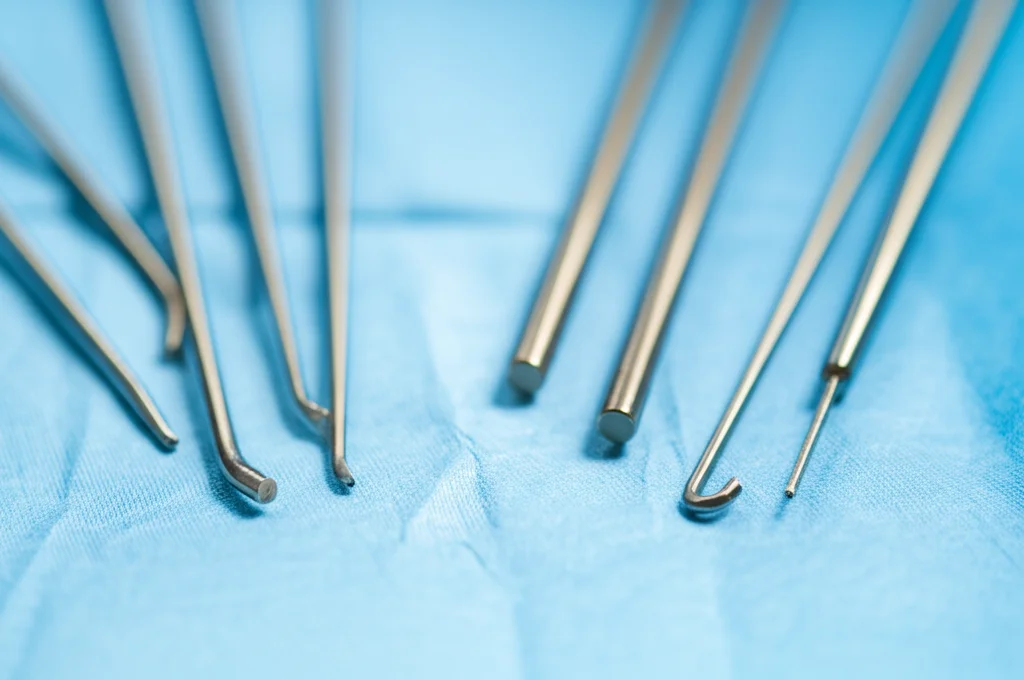 Fotografia macro di strumenti chirurgici per artroscopia della spalla disposti su un telo sterile blu, luce chirurgica intensa che crea riflessi metallici, messa a fuoco selettiva sulla punta di un trocar, obiettivo macro 100mm, alta definizione.