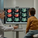 Grandangolo, obiettivo 20mm, che cattura un oftalmologo mentre spiega i risultati di scansioni oculari multimodali (come OCT/FFA) su un grande schermo a genitori preoccupati e al loro bambino in una clinica moderna e ben illuminata, messa a fuoco nitida sullo schermo e sull'interazione.