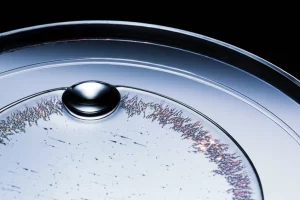 Immagine fotorealistica, obiettivo macro 80mm, che cattura l'interfaccia tra una sfera d'acciaio e un disco trasparente sotto pressione, un sottile film di lubrificante a base acquosa con strutture polimeriche visibili che brillano all'interno della zona di contatto EHL. Alto dettaglio, illuminazione controllata, focus sul contatto elasto-idrodinamico.