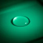 Immagine concettuale di un biosensore colorimetrico: una goccia di campione viene aggiunta a una striscia reattiva o a un pozzetto, provocando un cambiamento di colore visibile da incolore a blu-verde intenso, simboleggiando il rilevamento positivo di Shigella flexneri, stile macro fotografia 60mm, alta definizione, illuminazione drammatica.