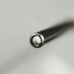 Fotografia still life di un elettrodo avanzato per pacemaker senza fili (LPM) caricato con il sistema RAPA-PLGA. Obiettivo macro 100mm, alta definizione, illuminazione laterale controllata per enfatizzare la texture metallica e il farmaco visibile nella cavità. Messa a fuoco selettiva sulla punta dell'elettrodo. Sfondo neutro sfocato.