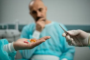 Immagine fotorealistica, obiettivo 35mm, profondità di campo accentuata. Un paziente con espressione pensierosa guarda due mani tese verso di lui: una mano tiene alcune pillole di antibiotico colorate, l'altra mano tiene delicatamente un piccolo strumento chirurgico sterile (es. una pinza laparoscopica sottile). Lo sfondo è neutro e leggermente sfocato. La scena rappresenta metaforicamente la scelta tra terapia antibiotica e intervento chirurgico per l'appendicite non complicata.