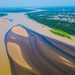 Veduta aerea del fiume Mahanadi in Odisha, India, che mostra la confluenza di acque più chiare e acque più scure provenienti da scarichi industriali o urbani lungo le rive. Obiettivo grandangolare 20mm, fotografia aerea, alta definizione, luce diurna.