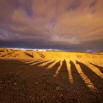 Immagine paesaggistica drammatica, obiettivo grandangolare 15mm, della Zona di Faglia Est Anatolica in Turchia al tramonto. Lunghe ombre proiettate sul terreno accidentato, cielo con nuvole minacciose dai colori caldi e freddi, messa a fuoco nitida che rivela la texture del paesaggio. Evoca la potenza sismica latente e il mistero storico legato al terremoto del 1513/1514. Lunga esposizione per accentuare il dramma.