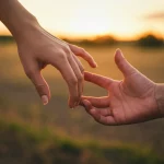 Immagine simbolica e realistica di due mani, una giovane e una adulta, che cercano di toccarsi ma sono separate da una distanza, su uno sfondo rurale sfocato al tramonto, rappresentando le difficoltà nella continuità delle cure per i giovani con autismo. Obiettivo 50mm, profondità di campo ridotta.