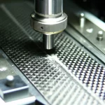 Immagine fotorealistica di un campione di laminato composito in fibra di carbonio [0/90/0/90]s montato su una macchina di prova universale durante un test di flessione a tre punti. Si vede chiaramente il punto di carico centrale e i due supporti. La luce da laboratorio evidenzia la trama della fibra di carbonio e un inizio di danneggiamento al centro del campione. Obiettivo prime 50mm, profondità di campo controllata.