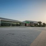 Vista esterna di una moderna scuola a energia zero a Dubai, illuminata dal sole, con pannelli solari visibili sul tetto e aree verdi circostanti. Wide-angle lens, 15mm, sharp focus, luce diurna intensa.