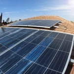 Installazione di pannelli solari fotovoltaici sul tetto di una casa residenziale in Giordania sotto un cielo azzurro e soleggiato. Ripresa leggermente dal basso con un obiettivo grandangolare 24mm per enfatizzare l'impianto e il cielo. Messa a fuoco nitida, luce diurna brillante.