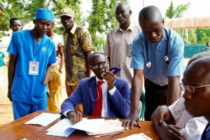 Fotografia concettuale, obiettivo 50mm con profondità di campo, che mostra diverse persone (un operatore sanitario locale, un funzionario governativo, un rappresentante di ONG) attorno a un tavolo in Liberia, le loro espressioni riflettono significati divergenti e tensioni di potere sottostanti, luce naturale filtrata.