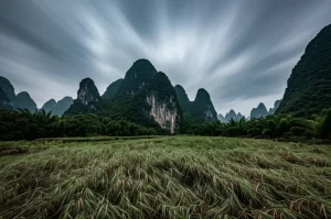 Paesaggio carsico mozzafiato della regione di Guangxi, Cina, con picchi calcarei iconici e vegetazione lussureggiante sotto un cielo drammatico, wide-angle lens, 15mm, sharp focus, long exposure per nuvole setose, evidenziando la fragilità dell'ecosistema minacciato dall'inquinamento da metalli pesanti.