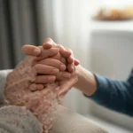 Primo piano di mani di un genitore che stringono delicatamente quelle di un figlio adolescente, luce calda e soffusa proveniente da una finestra laterale, obiettivo prime 50mm, profondità di campo ridotta per sfocare lo sfondo e concentrarsi sulle mani, trasmette supporto, connessione e calore emotivo.