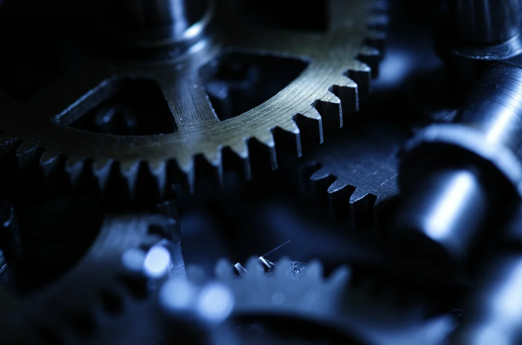 Fotografia macro di ingranaggi complessi e interconnessi, alcuni illuminati da una luce blu focalizzata che simboleggia l'ottimizzazione, altri in ombra. Profondità di campo ridotta, alta definizione, illuminazione drammatica, obiettivo macro 90mm.