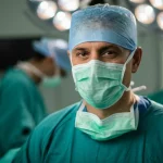 Ritratto fotografico di un chirurgo esperto e rassicurante che guarda in camera, simboleggiando la fiducia nella chirurgia oncologica anche in età avanzata. Luce morbida, profondità di campo, obiettivo prime 50mm, toni caldi e neutri.