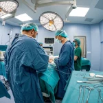 Immagine grandangolare di una sala operatoria pediatrica moderna e luminosa, con personale medico concentrato attorno a un tavolo operatorio durante un intervento delicato su un neonato. Messa a fuoco nitida, obiettivo grandangolare 18mm, che trasmette un senso di speranza, precisione e alta tecnologia medica.