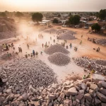 Panoramica fotorealistica di una vasta cava di granito artigianale a Ouagadougou, Burkina Faso. Lavoratori, principalmente donne, sparsi nell'area, intenti a spaccare e trasportare pietre con attrezzi manuali. Polvere e condizioni aride sotto un cielo africano. Obiettivo grandangolare 20mm, luce del tardo pomeriggio, alta definizione, stile documentario per catturare la scala e l'attività.