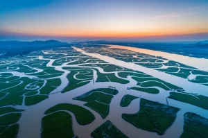 Veduta aerea mozzafiato della complessa rete di canali e specchi d'acqua nella pianura alluvionale del Fiume Yangtze e del Lago Poyang durante la stagione umida, fotografia paesaggistica grandangolare 10mm, lunga esposizione per acque setose, colori vividi all'alba.