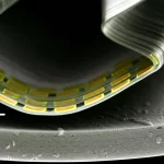 Immagine fotorealistica, obiettivo macro 60mm, di un transistor OECT all-gel estensibile piegato delicatamente su una superficie curva, illuminazione controllata per evidenziare la sua flessibilità intrinseca e la struttura interna del gel semiconduttore e dell'ionogel elettrolita, alta definizione dei dettagli.