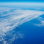 Vista aerea dell'Oceano Atlantico equatoriale con pattern di nuvole convettive (ITCZ) che si estendono sull'acqua blu profondo, evidenziando l'interazione atmosfera-oceano, obiettivo grandangolare 18mm, luce solare diffusa, messa a fuoco nitida sull'orizzonte.