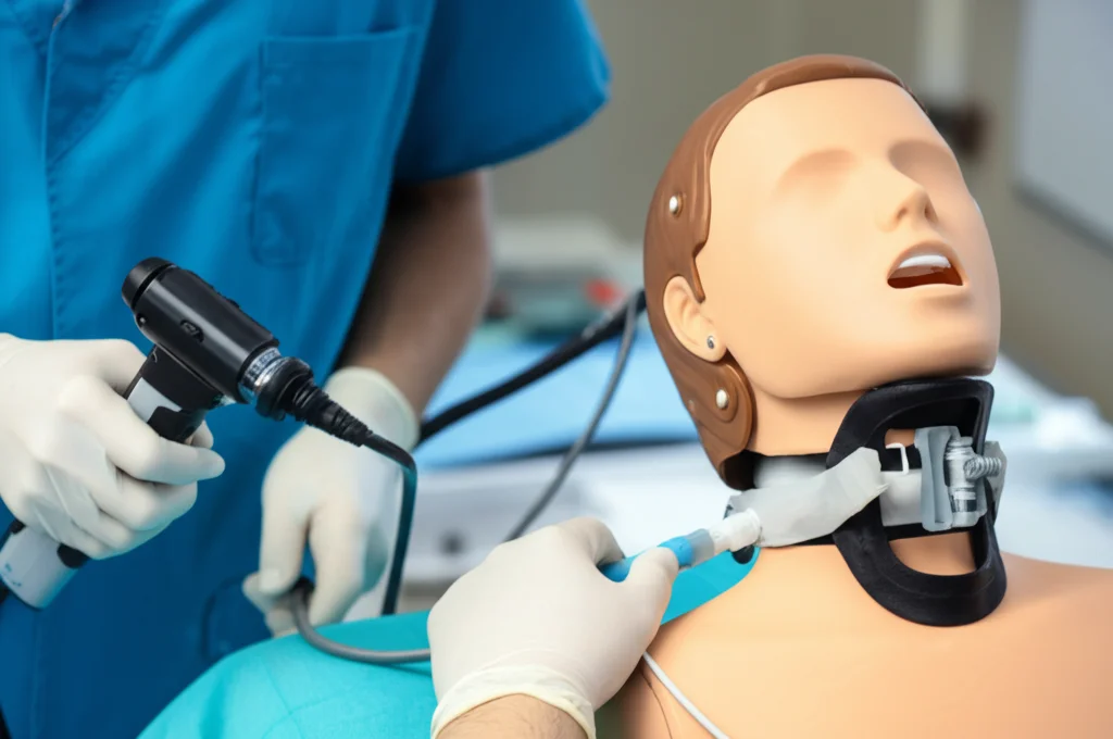 Fotografia macro di un operatore sanitario inesperto, concentrato mentre usa un videolaringoscopio AIRWAY SCOPE su un manichino per l'addestramento delle vie aeree in uno scenario di immobilizzazione cervicale, illuminazione controllata da studio, messa a fuoco precisa sul display del dispositivo e sulle mani guantate, obiettivo macro 85mm, alta definizione.