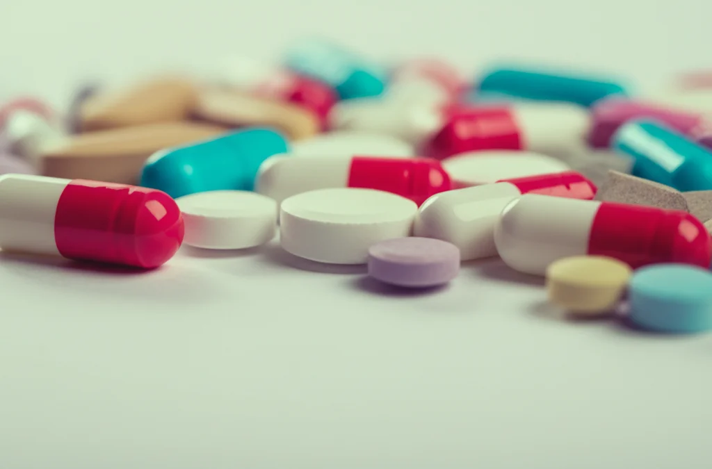 Primo piano di capsule e compresse farmaceutiche colorate sparse su uno sfondo neutro, obiettivo macro 100mm, messa a fuoco selettiva su una pillola, alta definizione, illuminazione morbida da studio.