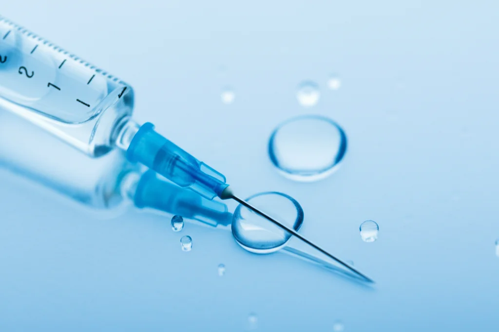 Fotografia macro, 70mm, di gocce di vaccino su una superficie sterile accanto a una siringa. Illuminazione da laboratorio controllata, alta definizione, focus preciso sulle gocce, sfondo leggermente sfocato.