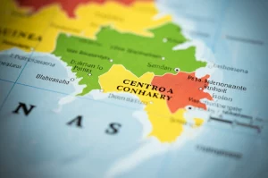 Mappa stilizzata ma fotorealistica della penisola di Conakry, Guinea, con sovrapposte zone colorate che indicano i tempi di percorrenza variabili (dal verde per breve al rosso per lungo) per raggiungere le strutture sanitarie per il parto, evidenziando le disparità tra centro e periferia. Macro lens, 80mm, high detail, controlled lighting on map texture, visualizzazione dati geografici.