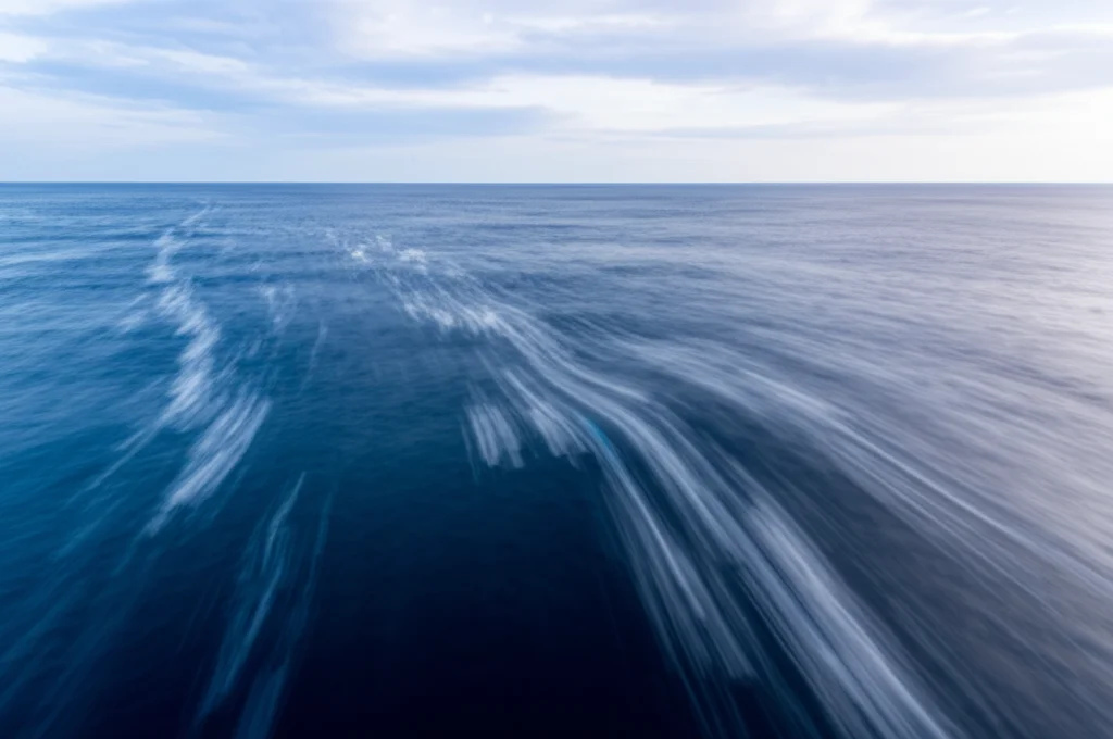Fotografia grandangolare, obiettivo 15mm, della corrente oceanica Kuroshio vicino alle isole Izu, Giappone. Acqua blu profondo con scie visibili della corrente, lunga esposizione per rendere l'acqua liscia ma mostrando il movimento, cielo parzialmente nuvoloso all'alba, messa a fuoco nitida sull'orizzonte marino.