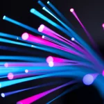 Visualizzazione artistica di impulsi luminosi che viaggiano ad altissima velocità attraverso i multipli core di una fibra ottica. Effetto motion blur per indicare velocità, colori vivaci (ciano, magenta) per rappresentare i dati, sfondo scuro high-tech. Teleobiettivo zoom 150mm, fast shutter speed per congelare parzialmente il movimento ma con scie luminose.