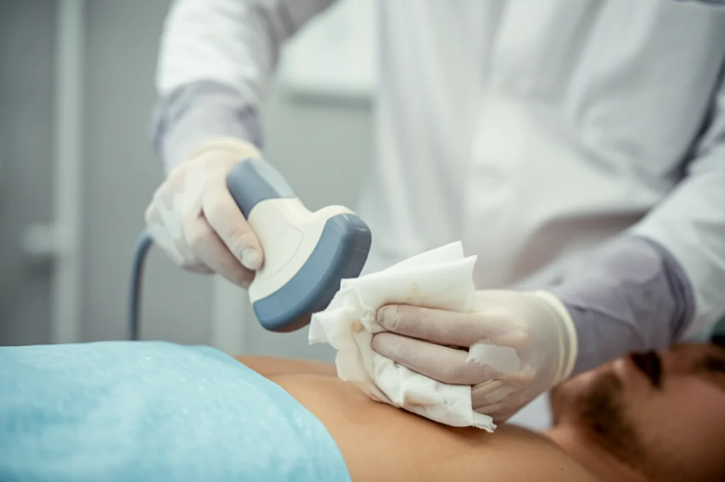 Primo piano, obiettivo prime 50mm, mano guantata che pulisce una sonda ecografica con una salvietta disinfettante, focus sulla testa della sonda, sfondo clinico leggermente sfocato, profondità di campo.