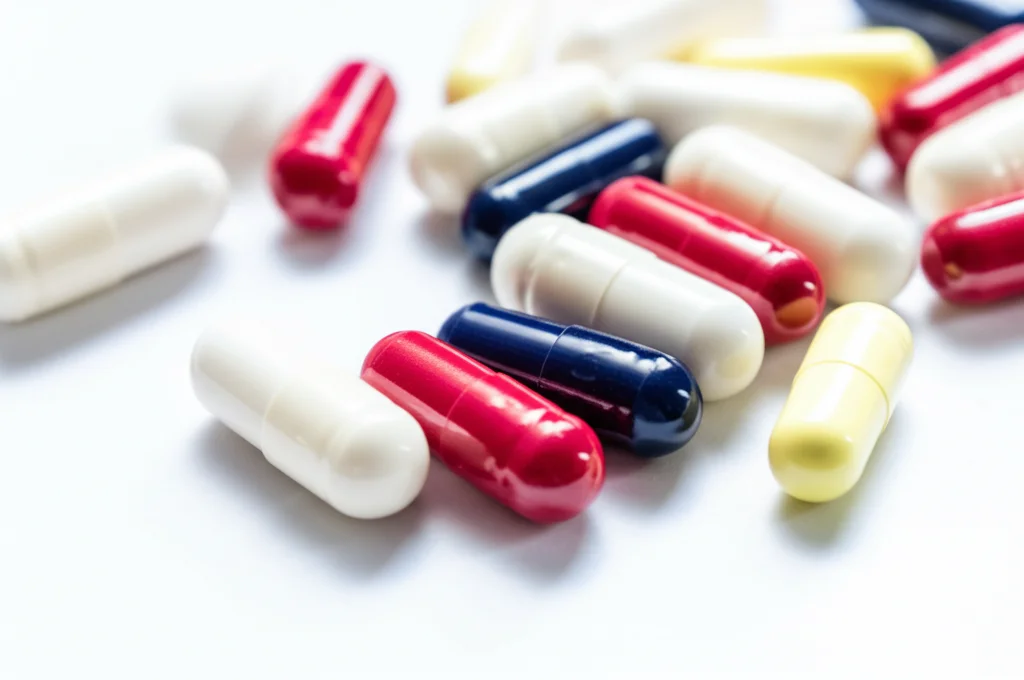 Primo piano di diverse capsule colorate di integratori alimentari per capelli, pelle e unghie sparse su una superficie bianca e pulita. Stile still life, lente macro 100mm, alta definizione dei dettagli delle capsule, illuminazione da studio controllata.