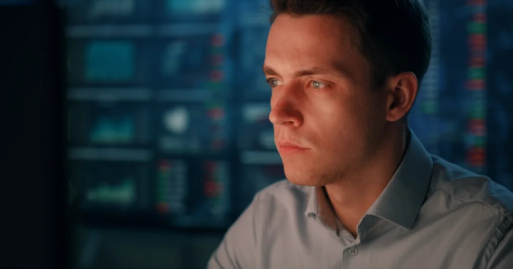 Un analista finanziario concentrato osserva uno schermo con grafici complessi di flussi di dati finanziari, cercando anomalie. Stile cinematografico, illuminazione d'atmosfera con contrasti netti, obiettivo 50mm, profondità di campo ridotta.