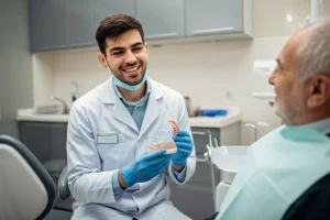 Fotografia di ritratto, un dentista sorridente (studente) che mostra una protesi completa rimovibile a un paziente anziano sereno, studio dentistico luminoso, prime lens 35mm, profondità di campo accentuata, toni caldi.