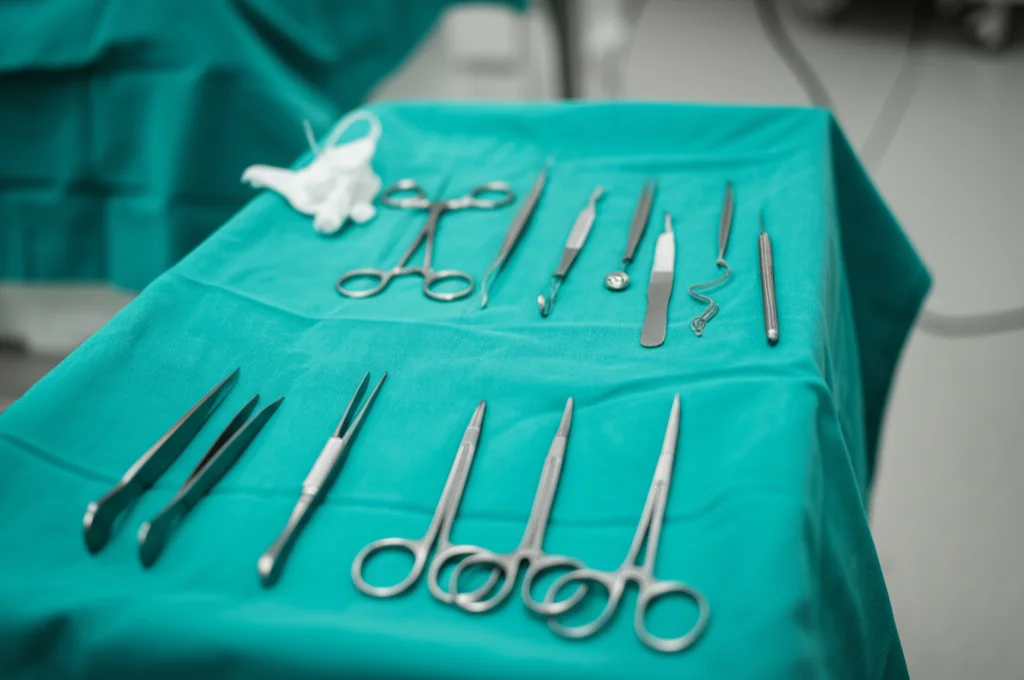 Immagine macro di strumenti chirurgici di precisione, come pinze e bisturi, appoggiati su un telo sterile verde in una sala operatoria moderna. L'illuminazione è controllata e focalizzata sugli strumenti, mettendo in risalto i dettagli metallici. Obiettivo macro 100mm, alta definizione, focus selettivo.