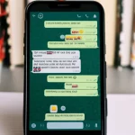 Immagine fotorealistica, primo piano di uno smartphone che mostra una chat di gruppo WhatsApp con messaggi relativi all'apprendimento dell'inglese, sfondo sfocato di libri e appunti, obiettivo macro 60mm, alta definizione, messa a fuoco precisa.