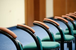 Immagine simbolica del dissenso istituzionale: una sedia vuota leggermente discostata da una fila di sedie identiche in una sala riunioni formale, luce direzionale che evidenzia la sedia vuota, obiettivo 50mm, profondità di campo ridotta.