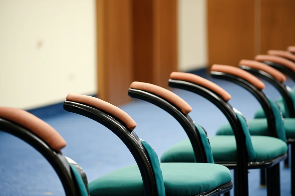 Immagine simbolica del dissenso istituzionale: una sedia vuota leggermente discostata da una fila di sedie identiche in una sala riunioni formale, luce direzionale che evidenzia la sedia vuota, obiettivo 50mm, profondità di campo ridotta.