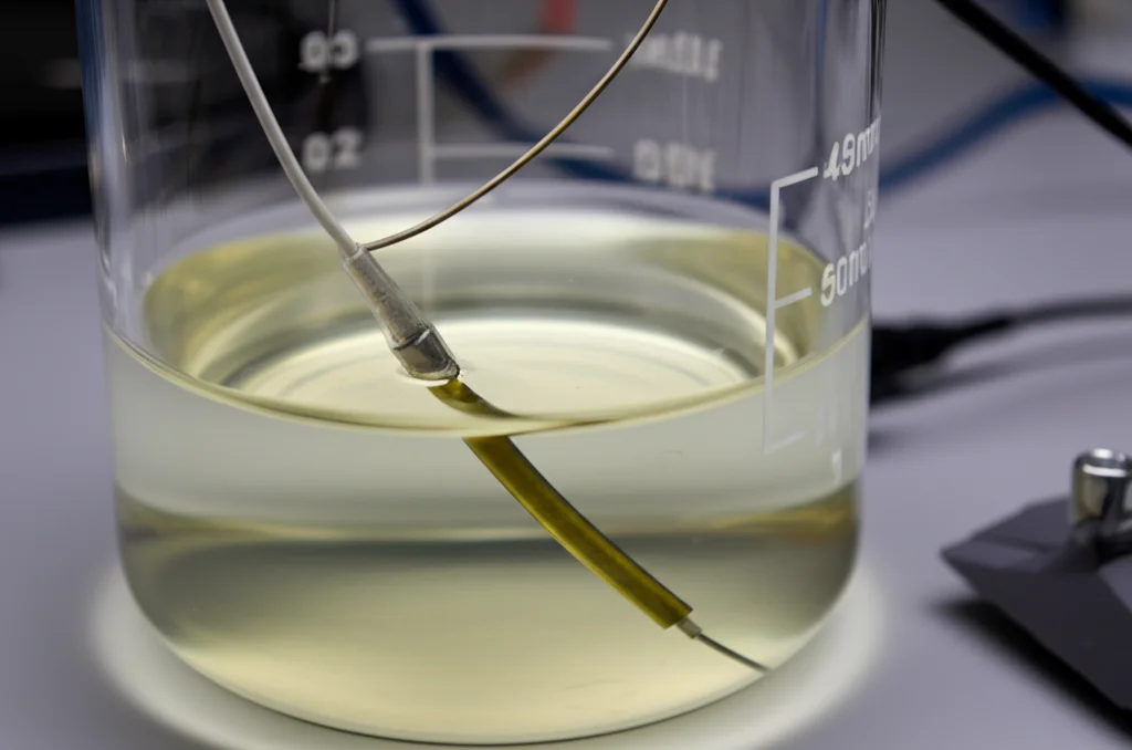 Setup di laboratorio, natura morta, lente macro 60mm, messa a fuoco precisa, che mostra un campione TI-6AL-4V immerso in un becher con soluzione salina tamponata con fosfato (PBS) collegata agli elettrodi per la spettroscopia di impedenza elettrochimica (EIS), simulando le condizioni del fluido corporeo.