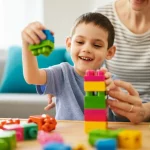 Immagine fotorealistica di un bambino sorridente con paralisi cerebrale atassica che gioca con blocchi colorati, assistito da un adulto in un ambiente luminoso e accogliente. Obiettivo 50mm, luce naturale, profondità di campo media per mostrare interazione e ambiente.