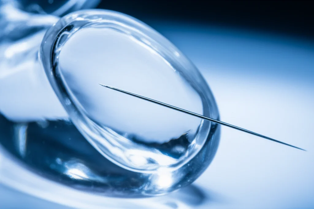 Fotografia macro di un ago da biopsia posizionato delicatamente accanto a un modello 3D trasparente di una prostata. Illuminazione da studio controllata per evidenziare i dettagli dell'ago e la struttura interna del modello. Obiettivo macro 100mm, alta definizione, messa a fuoco precisa sulla punta dell'ago.