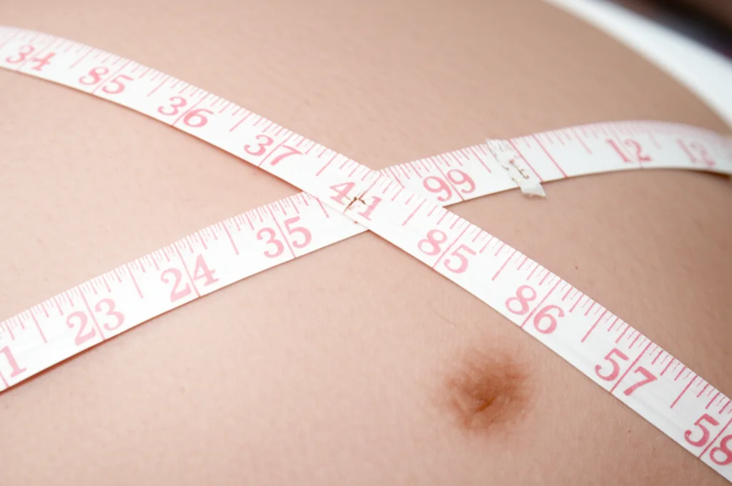 Immagine macro di un metro a nastro medico appoggiato delicatamente su un pancione, simboleggiando la misurazione della crescita fetale, obiettivo macro 90mm, alta definizione, illuminazione controllata.