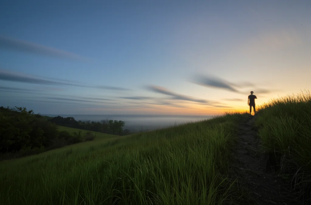 Fotografia grandangolare di un paesaggio sereno all'alba, con una persona in lontananza che cammina su un sentiero verso il sole nascente. Obiettivo grandangolare 10mm, lunga esposizione per nuvole soffuse, messa a fuoco nitida sul paesaggio.