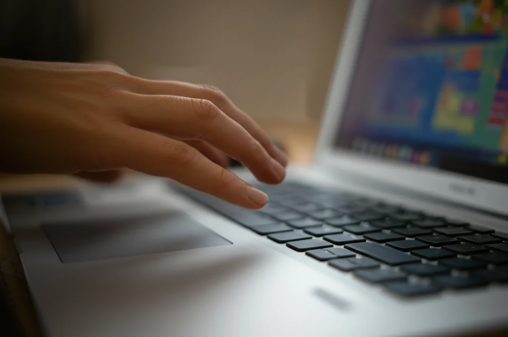 Immagine macro di una mano che digita su una tastiera di laptop, lo schermo mostra l'interfaccia colorata e accogliente di un programma online per genitori, illuminazione controllata e messa a fuoco precisa sui tasti, obiettivo macro 85mm.