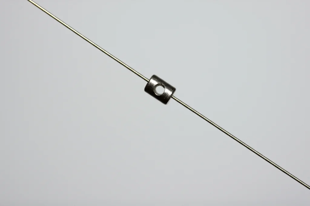 Fotografia macro ad alta definizione di un piccolo ancoraggio chirurgico in titanio (1mm x 10mm) collegato da un sottile filamento di acciaio inossidabile. Macro lens, 100mm, high detail, precise focusing, controlled studio lighting su sfondo neutro.