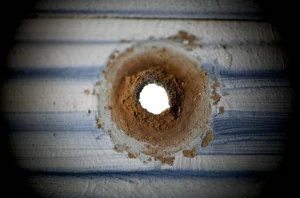 Immagine fotorealistica in primo piano, obiettivo macro 60mm, alto dettaglio, illuminazione controllata, focalizzata su un foro di perforazione causato da corrosione per pitting su una piastra corrugata di scambiatore di calore in acciaio inossidabile 316. Sono visibili sottili segni di depositi circostanti.