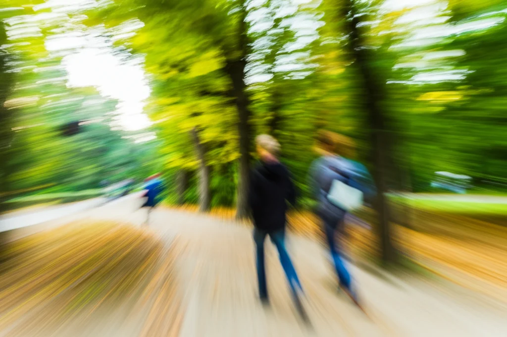 Fotografia di persone che camminano lungo un sentiero alberato in un parco cittadino polacco, teleobiettivo zoom 100mm, inseguimento del movimento leggero per catturare l'azione, luce naturale filtrata dalle foglie autunnali.
