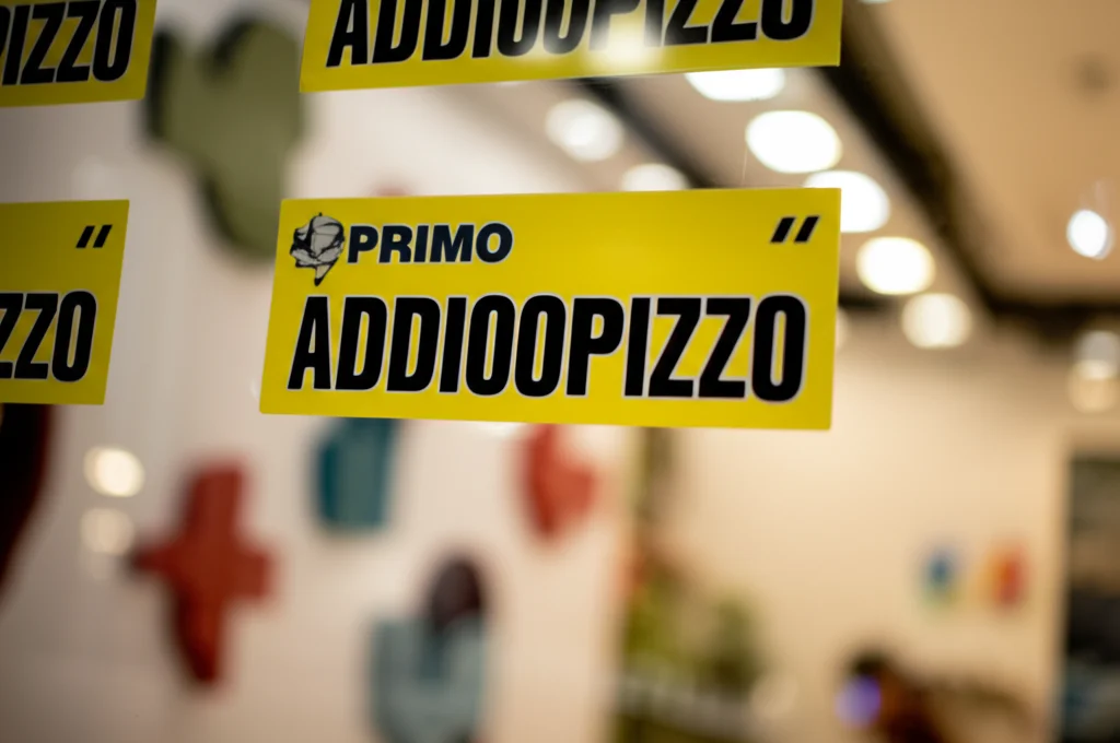 Primo piano di adesivi 'Addiopizzo' sulla vetrina di un negozio moderno e luminoso a Palermo, obiettivo macro 100mm, alta definizione, luce controllata, simbolo di resistenza civile e consumo critico.