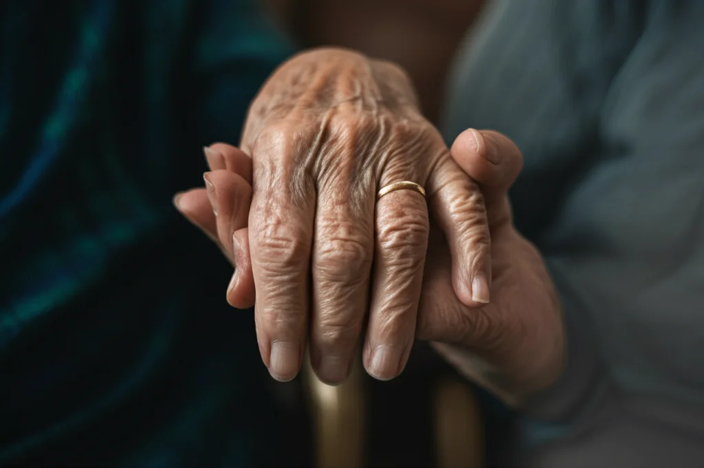 Primo piano macro di due mani anziane che si stringono delicatamente, simbolo di supporto e conforto; macro lens 90mm, alta definizione, illuminazione controllata morbida.